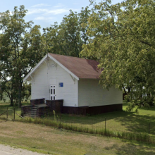 Front and side of the white schoolhouse on a brick base
