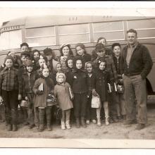 Photo of a group of school children with a bus driver in front of a bus.