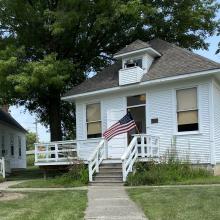 White schoolhouse with a flag, bell, and porch